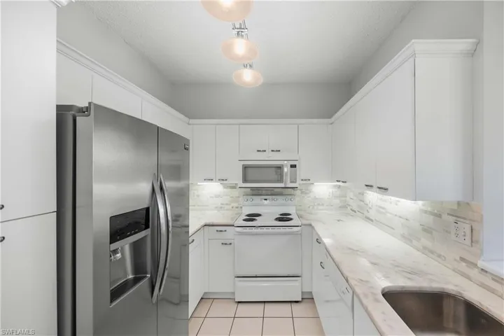Kitchen with white appliances, light tile patterned flooring, tasteful backsplash, white cabinetry, and a textured ceiling