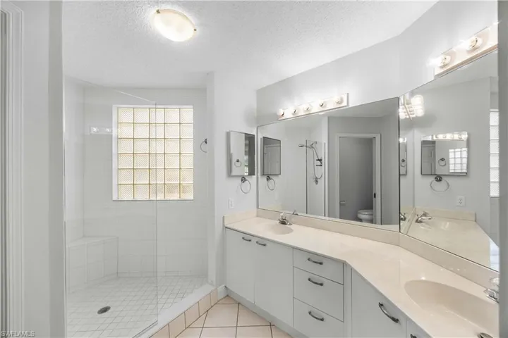 Bathroom featuring walk in shower, double vanity, a textured ceiling, and light tile patterned flooring