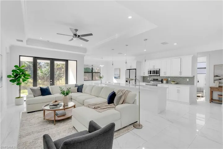 Living room featuring a ceiling fan, recessed lighting, light marble finish floors, a tray ceiling, and ornamental molding