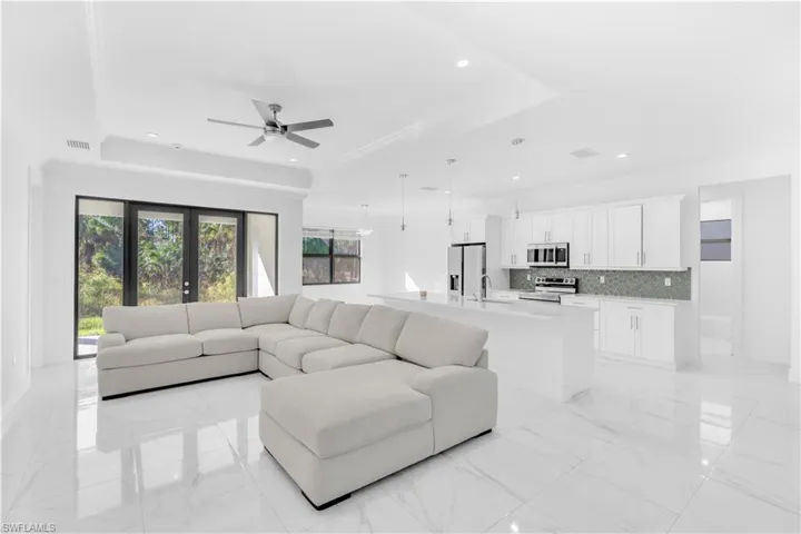 Living room with ornamental molding, ceiling fan, recessed lighting, a tray ceiling, and light marble finish flooring