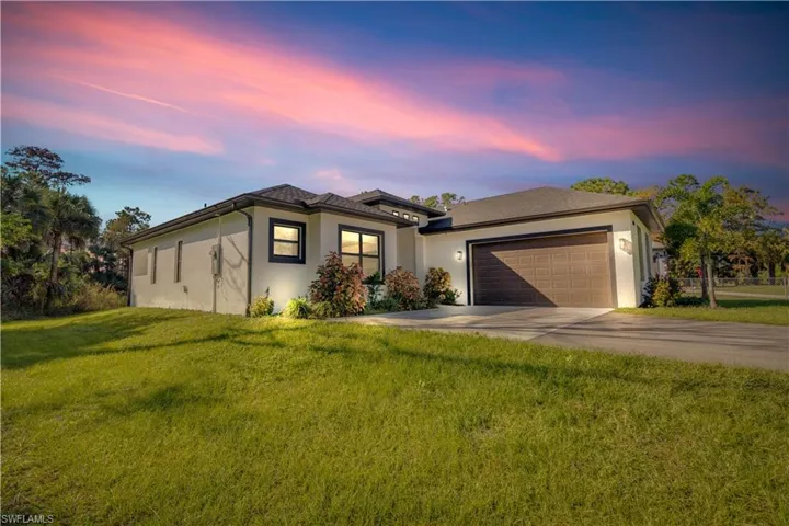 View of front of home featuring stucco siding, driveway, a front yard, and an attached garage