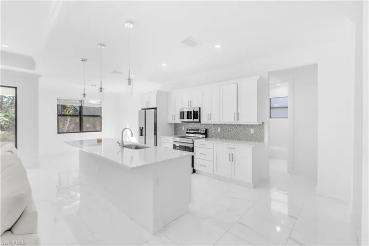 Kitchen featuring crown molding, appliances with stainless steel finishes, a kitchen island with sink, hanging light fixtures, and light marble finish floors