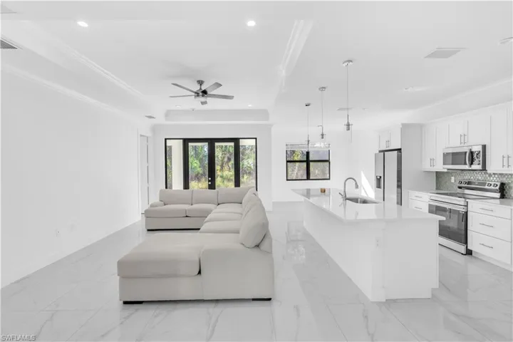 Living room with recessed lighting, light marble finish flooring, ornamental molding, ceiling fan, and a raised ceiling