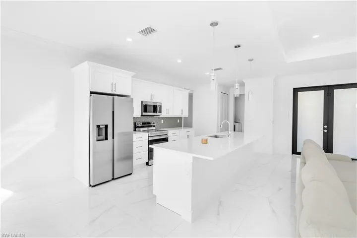 Kitchen with ornamental molding, stainless steel appliances, white cabinets, hanging light fixtures, and light marble finish floors