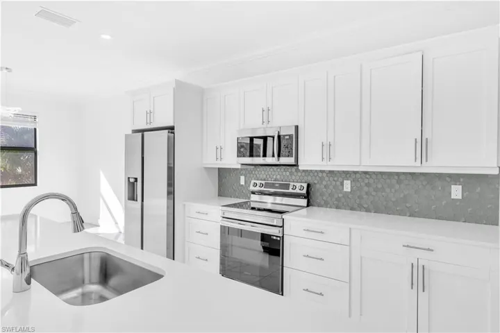 Kitchen with appliances with stainless steel finishes, white cabinetry, pendant lighting, tasteful backsplash, and crown molding