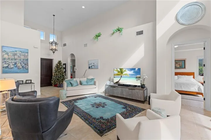 Living room with a towering ceiling, an inviting chandelier, plenty of natural light, and light tile patterned flooring