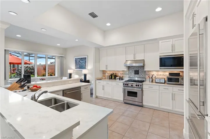 Kitchen with light stone countertops, sink, white cabinets, and high end appliances