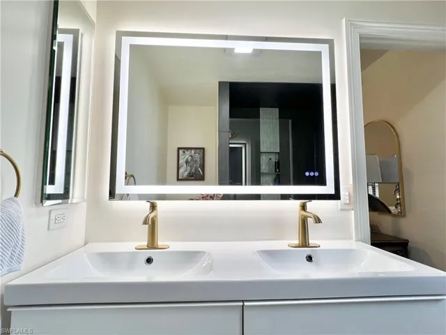 Double vanity with integrated sinks, illuminated mirror, brass-finish faucets, and white cabinetry