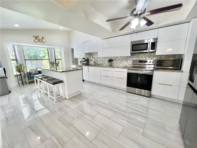 Modern kitchen featuring white cabinetry, stainless steel appliances, a center island with granite countertop, decorative backsplash, and wood-finish flooring