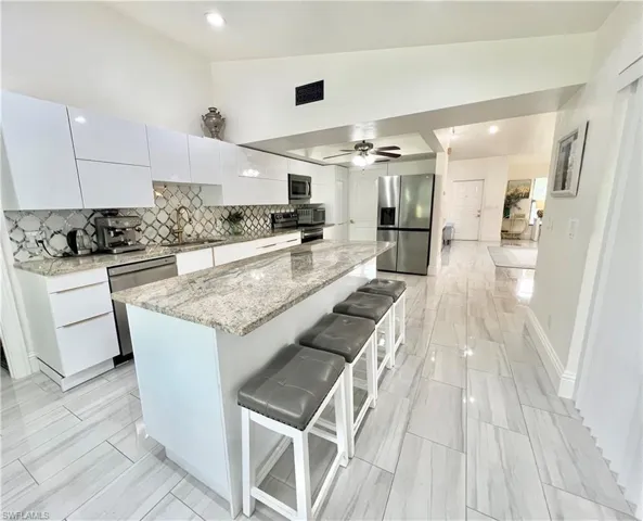 Contemporary kitchen featuring an expansive island with a granite countertop, stainless steel appliances, and sleek white cabinetry