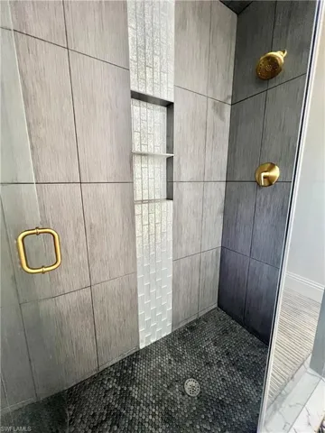 Walk-in shower featuring large format wall tiles, a mosaic tile accent strip, and a pebble-style floor