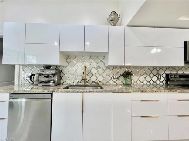 Modern kitchen featuring white high-gloss cabinetry with brass hardware, granite countertops, an arabesque tile backsplash, a stainless steel sink with a brass faucet, and a stainless steel dishwasher