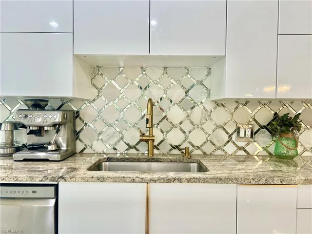 Kitchen featuring a geometric mosaic tile backsplash, white flat-panel cabinetry, granite countertops, and a gold-toned faucet