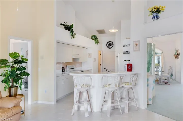 Kitchen with a kitchen breakfast bar, high vaulted ceiling, light countertops, hanging light fixtures, and white cabinetry
