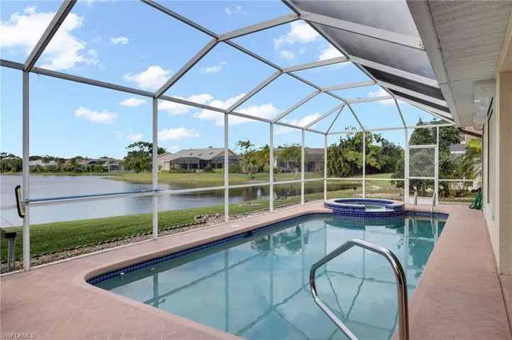 View of swimming pool featuring a sunroom, a lanai, a water view, a pool with connected hot tub, and a lawn