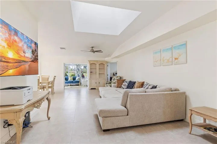 Tiled living room featuring ceiling fan and lofted ceiling with skylight