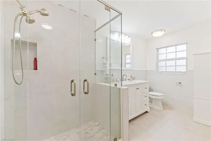 Updated Guest Bathroom featuring tile patterned floors, vanity, tile walls, toilet, and a shower with shower door
