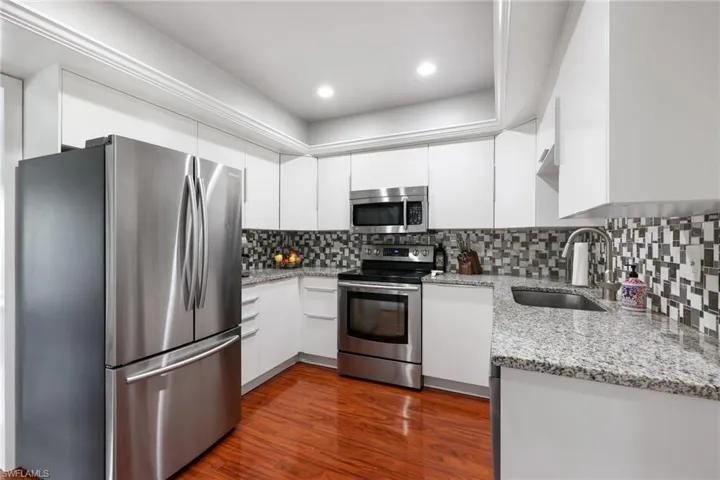 Kitchen with light stone counters, dark wood-style flooring, stainless steel appliances, white cabinets, and a sink