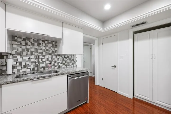 Kitchen featuring dishwasher, dark wood-style floors, light stone countertops, white cabinetry, and a sink