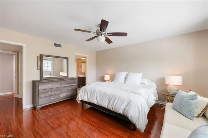 Bedroom with dark wood finished floors, baseboards, visible vents, a ceiling fan, and ensuite bath