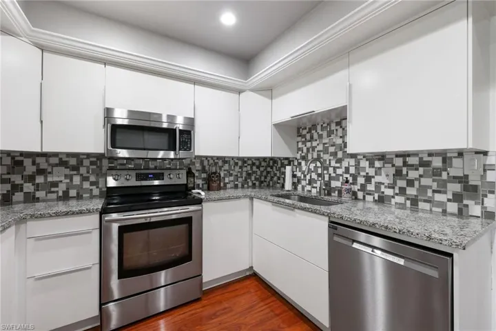 Kitchen featuring dark wood finished floors, appliances with stainless steel finishes, white cabinets, a sink, and light stone countertops
