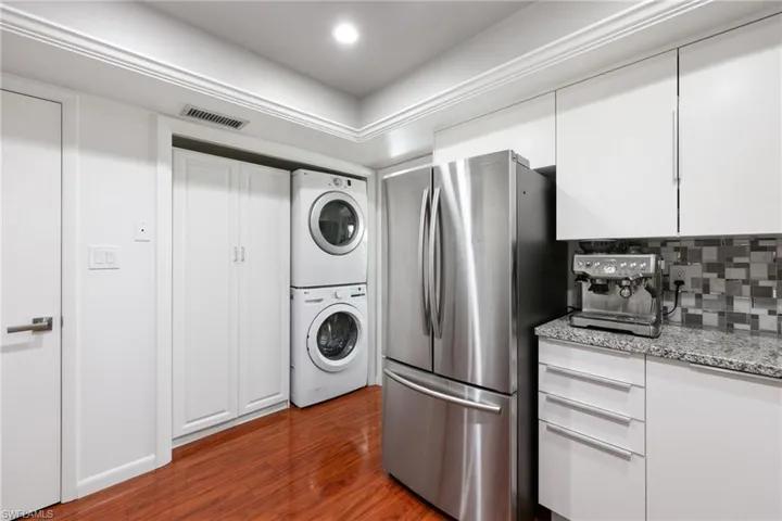 Kitchen featuring stacked washing maching and dryer, visible vents, white cabinets, and freestanding refrigerator