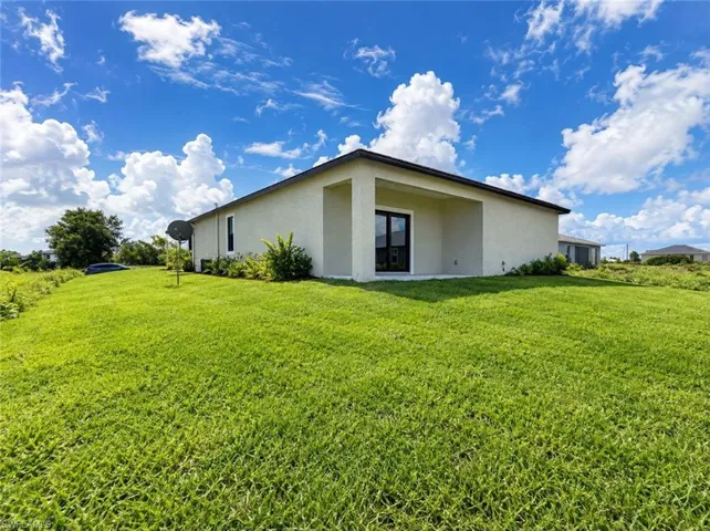 Exterior stucco finish, covered patio, black-framed sliding glass door, and expansive green lawn