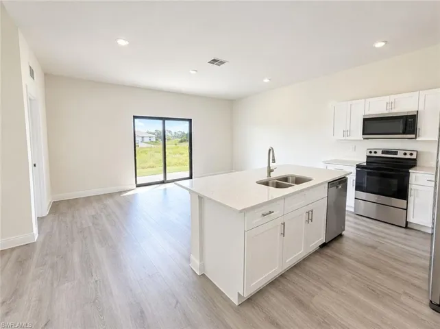 Open-concept kitchen with a central island, stainless steel appliances, white cabinetry, and wood-finish flooring