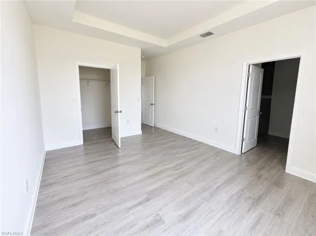 Recessed ceiling detail, wood-finish flooring, white trim, paneled interior doors, and a closet with wire shelving