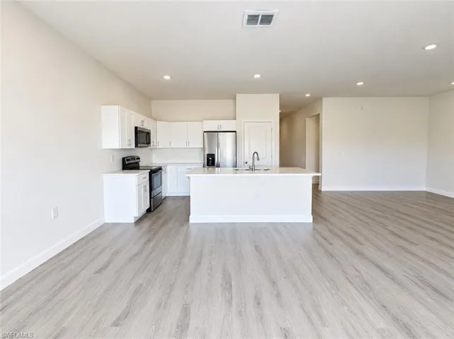 Open-concept kitchen featuring white cabinetry, stainless steel appliances, and a central island with an integrated sink