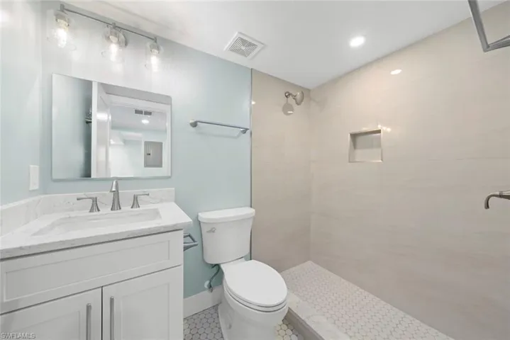 Bathroom featuring a white vanity with a marble countertop, a toilet, a walk-in shower with light-colored tile walls, and hexagonal floor tiling