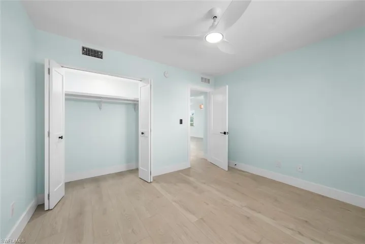 This room features light-colored walls, light wood-look flooring, and a ceiling fan with an integrated light