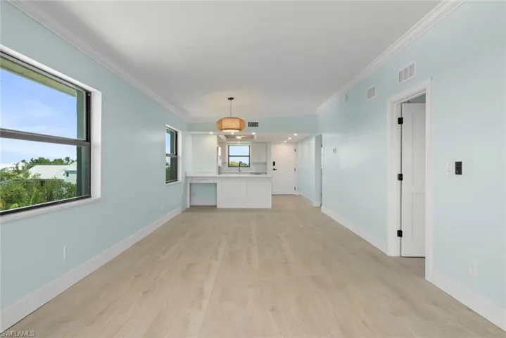 Expansive living area with light wood-style flooring, light blue walls, and multiple windows providing natural light