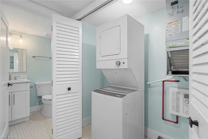 This space features a stacked washer and dryer, a vanity with a white countertop and sink, and a toilet