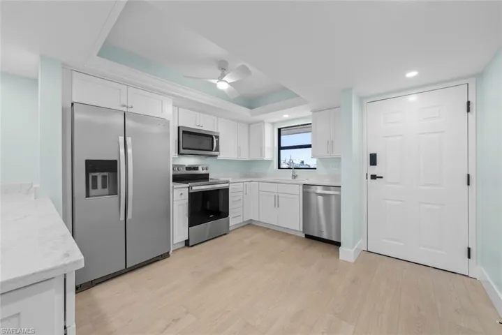 The kitchen features white cabinetry, stainless steel appliances, light-toned flooring, and a ceiling fan