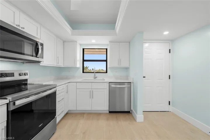 The kitchen features white cabinetry, stainless steel appliances, light-colored countertops, and a window above the sink