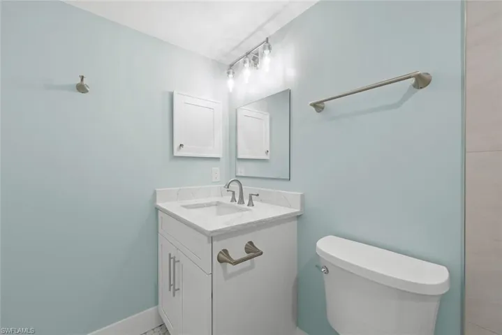 Bathroom featuring a white vanity with a marble countertop and a single basin sink, a toilet, and a wall-mounted mirror with a medicine cabinet