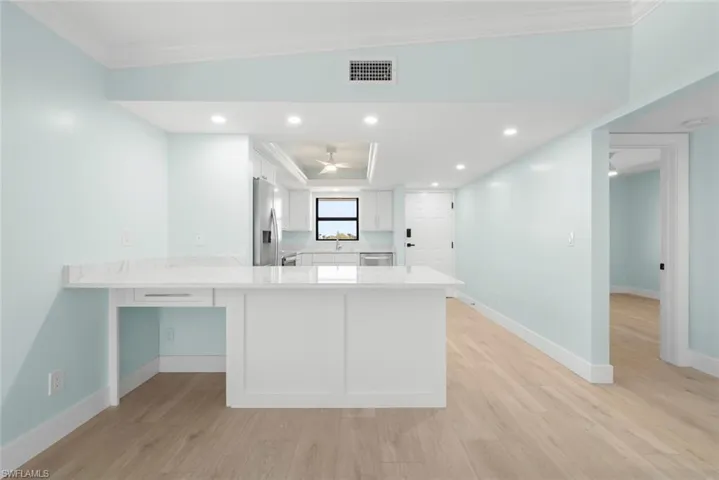 Open concept living space featuring light wood-style flooring, a kitchen with white cabinetry and stainless steel appliances, and a central island with a light-colored countertop