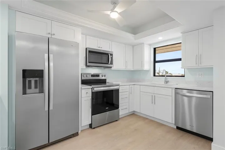 The kitchen features white cabinetry, stainless steel appliances, light-colored countertops, and a window with a view