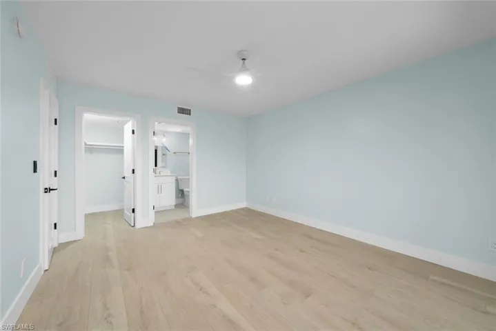 This bright room features light-colored walls, light wood flooring, and a ceiling fan
