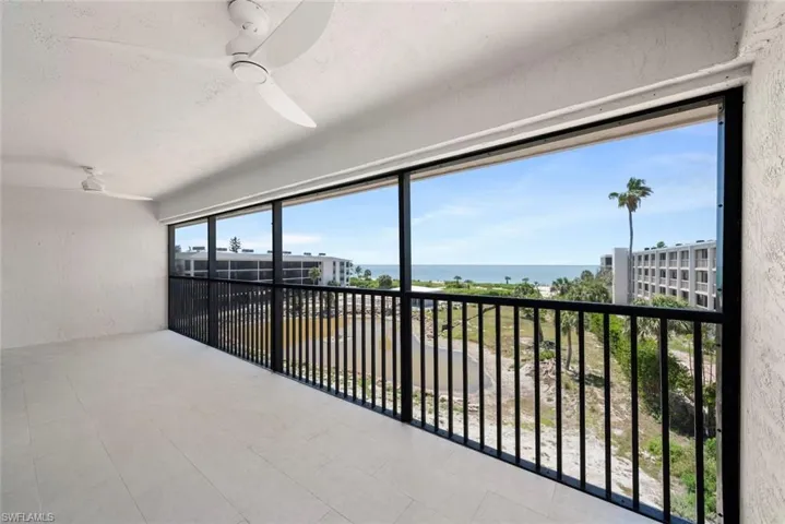 Expansive balcony with tiled flooring, equipped with ceiling fans, and offering views of the ocean and nearby structures