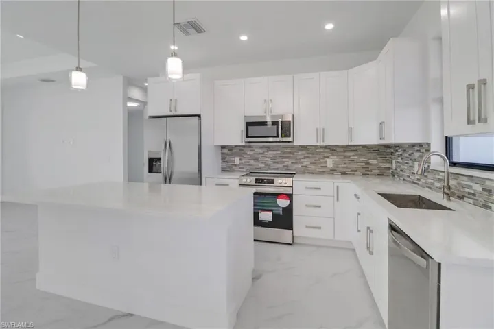 Kitchen featuring sink, pendant lighting, a kitchen island, stainless steel appliances, and white cabinets