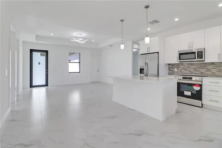 Kitchen featuring white cabinets, a center island, appliances with stainless steel finishes, and pendant lighting