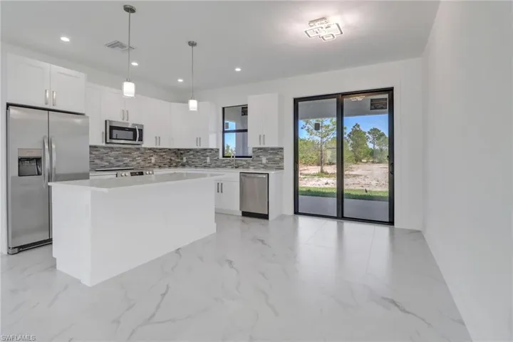 Kitchen featuring white cabinetry, a kitchen island, stainless steel appliances, hanging light fixtures, and tasteful backsplash