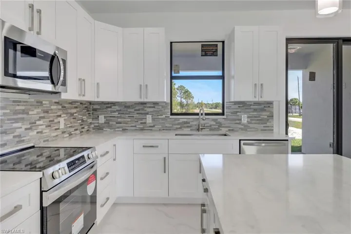 Kitchen featuring white cabinetry, stainless steel appliances, light stone countertops, sink, and decorative backsplash