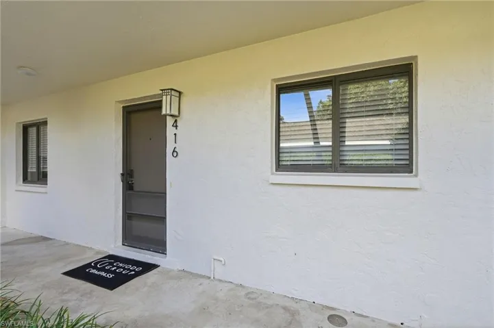 Exterior entry featuring a textured stucco facade, dark-frame sliding windows, a glass-panel storm door, and a wall-mounted lantern light fixture