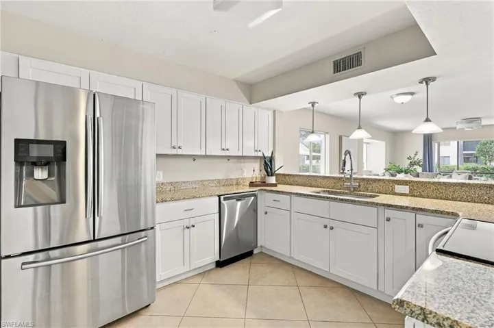 Kitchen featuring white shaker-style cabinetry, stone-finish countertops, stainless steel appliances, tile flooring, and pendant lighting