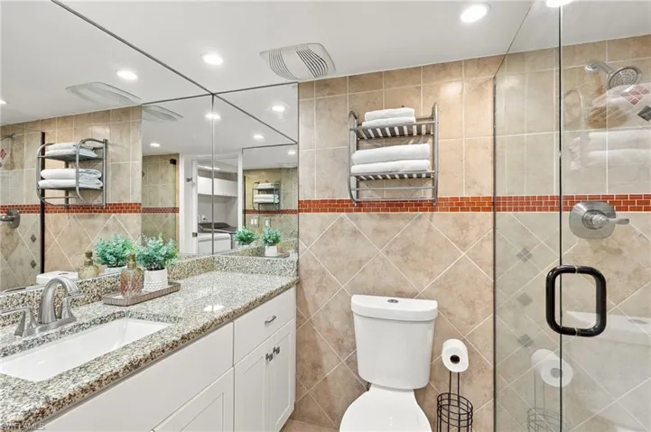 Bathroom featuring a granite-top vanity, wall-to-wall mirror, recessed lighting, and a glass-enclosed shower with decorative tile accents