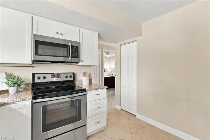 Kitchen featuring white shaker-style cabinetry, speckled stone-finish countertops, stainless steel microwave, stainless steel range, and tile flooring