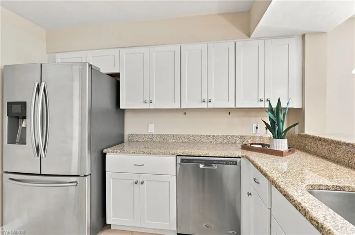 Kitchen featuring white shaker-style cabinetry, speckled stone countertops, and stainless steel appliances including a French-door refrigerator and dishwasher